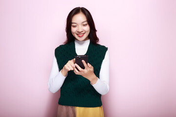 A woman has a pink background as a backdrop for a single portrait, smiling and holding a cell phone...