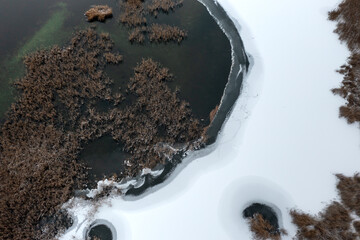 Beautiful winter aerial landscape. A lake with a semi-frozen coast covered in snow and dried water...