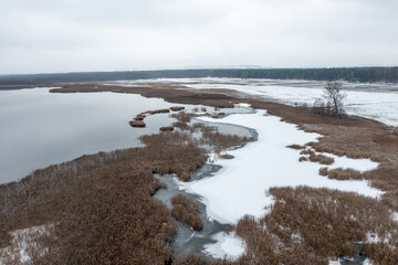 Beautiful winter aerial landscape. A lake with a frozen coast covered in snow and a forest on the horizon.