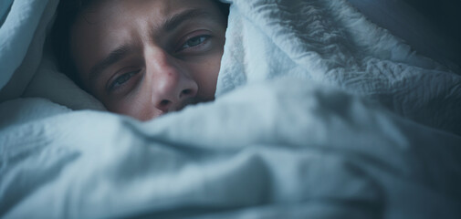Sick man lying in bed under blanket and looking at camera.
