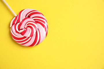 Stick with colorful lollipop swirl on yellow background, top view. Space for text