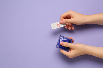 Woman holding condom and contraceptive pills on violet background, top view with space for text....