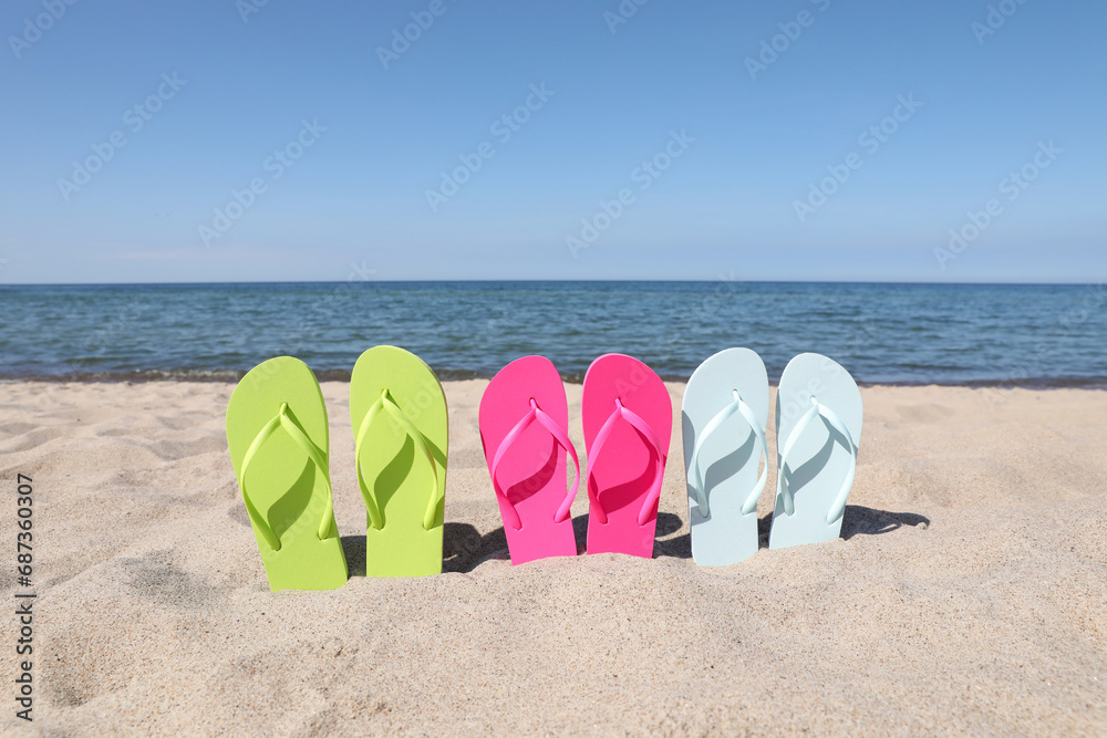 Sticker Stylish colorful flip flops on beach sand