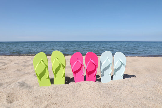 Stylish colorful flip flops on beach sand