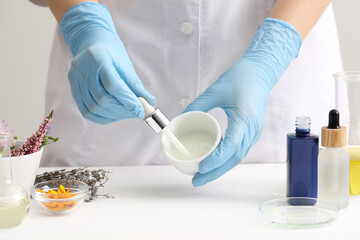 Scientist developing cosmetic oil at white table, closeup