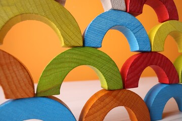 Colorful wooden pieces of educational toy on light table against orange wall, closeup. Motor skills...
