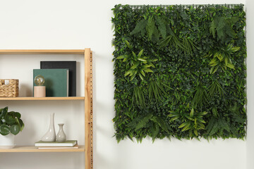 Green artificial plant panel on white wall and shelving unit with decorative elements in room
