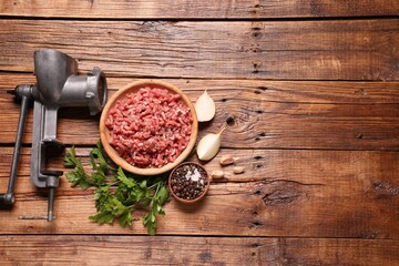 Manual meat grinder with beef mince, peppercorns, onion and parsley on wooden table, flat lay....