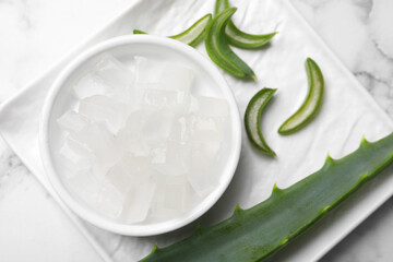 Aloe vera gel and slices of plant on white marble table, top view