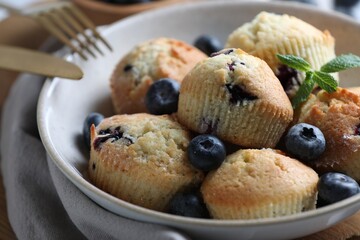 Delicious muffins with blueberries and mint in bowl on table, closeup