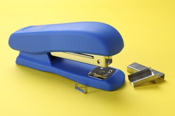 Blue stapler with staples on yellow background