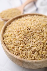 Raw bulgur in bowl on table, closeup