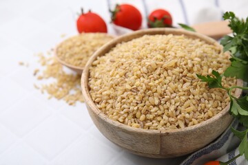 Raw bulgur in bowl and parsley on white table, closeup