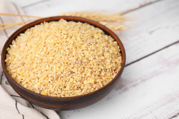 Raw bulgur in bowl on white wooden table, closeup