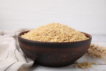Raw bulgur in bowl on white wooden table, closeup