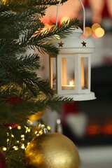 Christmas lantern with burning candle on fir tree against blurred background, closeup