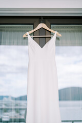 Wedding dress hangs on the glass door of a balcony with the reflection of the sea and mountains