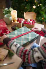 Young asian woman in sweater wrapping christmas gift and decorating with red ribbon while preparing toys ornaments and presents to celebrate for christmas festive holiday and winter seasons at house