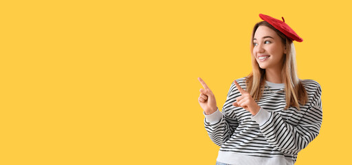 Young woman pointing at something on yellow background with space for text