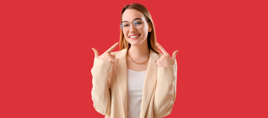 Young businesswoman pointing at her smile on red background