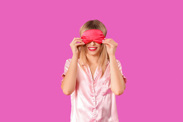 Young woman in pajamas with sleeping mask on purple background