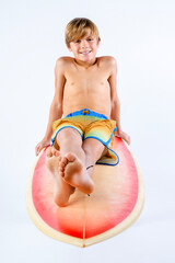 Smiling cute surfer boy barefoot in colorful board shorts sitting on his surfboard © 3Days2Go Media
