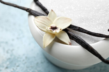 Fototapeta na wymiar Bowl with aromatic vanilla sugar, flower and sticks on blue background