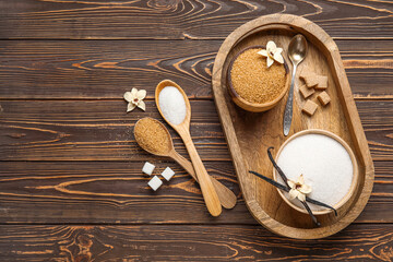 Bowls and spoons of aromatic vanilla sugar, flowers with sticks on wooden background