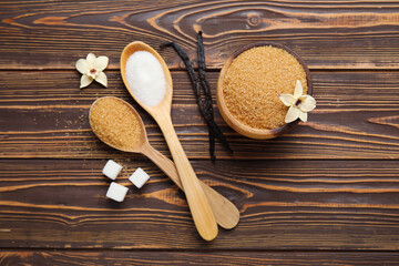 Fototapeta na wymiar Bowl and spoons of aromatic vanilla sugar, flowers with sticks on wooden background
