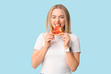 Young woman eating piece of tasty pizza on blue background