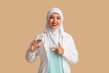 Female Muslim doctor in hijab with ampule on beige background. World Hijab Day concept