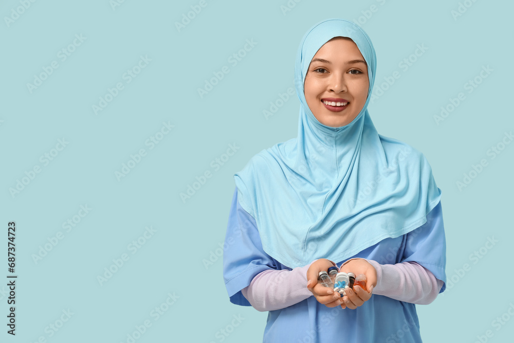 Sticker Female Muslim doctor in hijab with pills and ampules on blue background. World Hijab Day concept