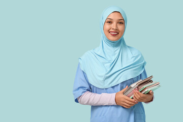 Female Muslim doctor in hijab with journals on blue background. World Hijab Day concept