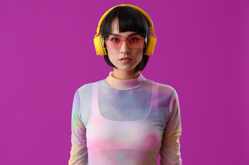 Beautiful young stylish woman in sunglasses with headphones on purple background