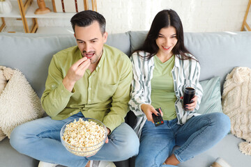 Young couple with popcorn and cola watching TV at home
