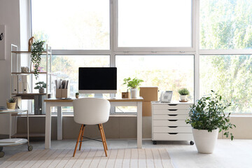 Interior of modern office with workplace, shelf unit and plants