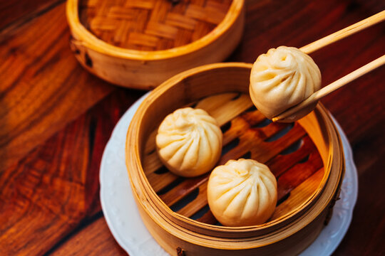 freshly cooked bao held over a wooden steamer by chopsticks at a table