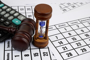 Judge gavel and calculator with hourglass on calendar pages background. 