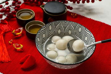 Bowl of tangyuan, tea and Chinese decor on red mat, closeup. Dongzhi Festival