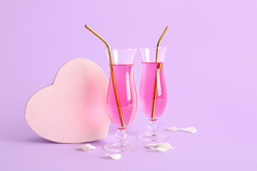 Glasses of tasty cocktail with decorative heart and rose petals on lilac background. Valentine's Day celebration