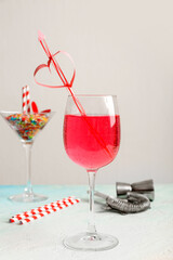 Glass of tasty cocktail with straw and bartender tools on blue grunge table against white background. Valentine's Day celebration