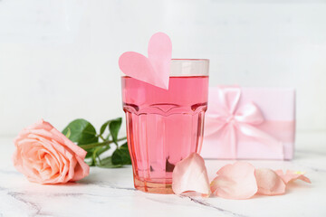 Glass of tasty cocktail with gift and rose on grunge table against white wooden background. Valentine's Day celebration