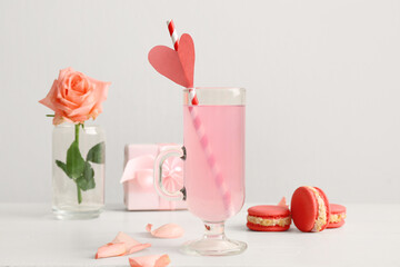 Glass of tasty cocktail with cakes and rose on wooden table against white background. Valentine's Day celebration