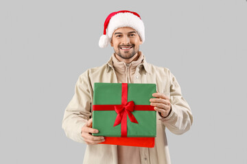 Handsome man in Santa hat with Christmas present on light background