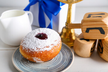 Tasty donut, milk and dreidels for Hanukkah celebration on light wooden table, closeup