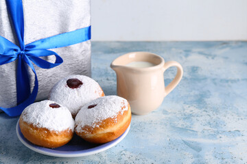 Plate with tasty donuts, milk and gift for Hanukkah celebration on color table