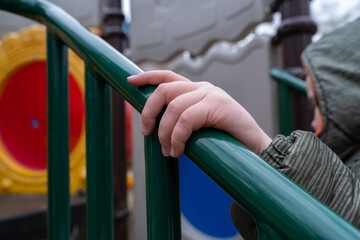 Boy goes up the stairs at the playground and holds on to the railing