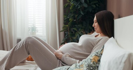 Pregnant woman in comfortable and fashionable pajamas, her hand resting on her belly as she connects with her baby in a moment of pure bliss.