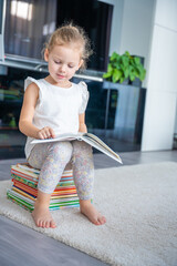 Cute Little girl is sitting on stack of children's books and leafing through a book with fairy tales