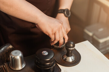 Closeup hand of barista preparation tampering ground coffee in portafilter for espresso machine. Coffee making concept.
